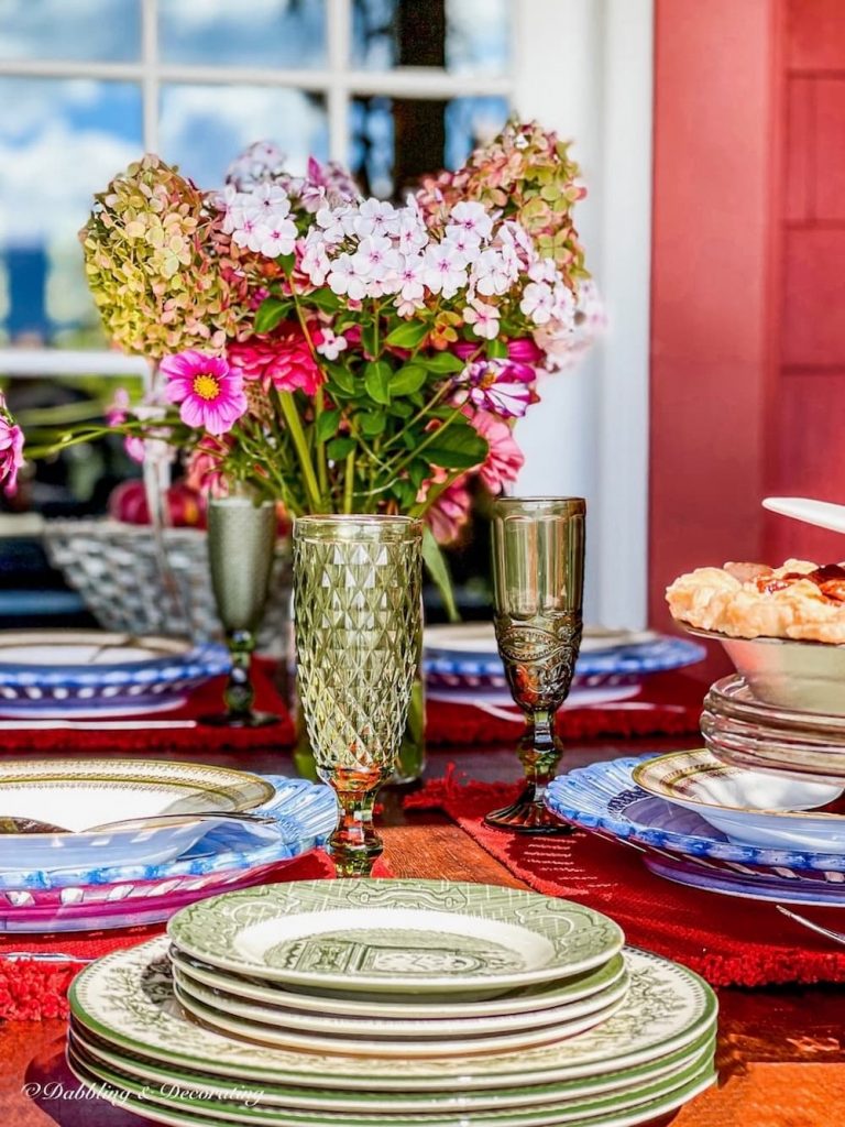 Vintage table setting with fall flowers in mason jar on porch table setting with green and white vintage dishes.