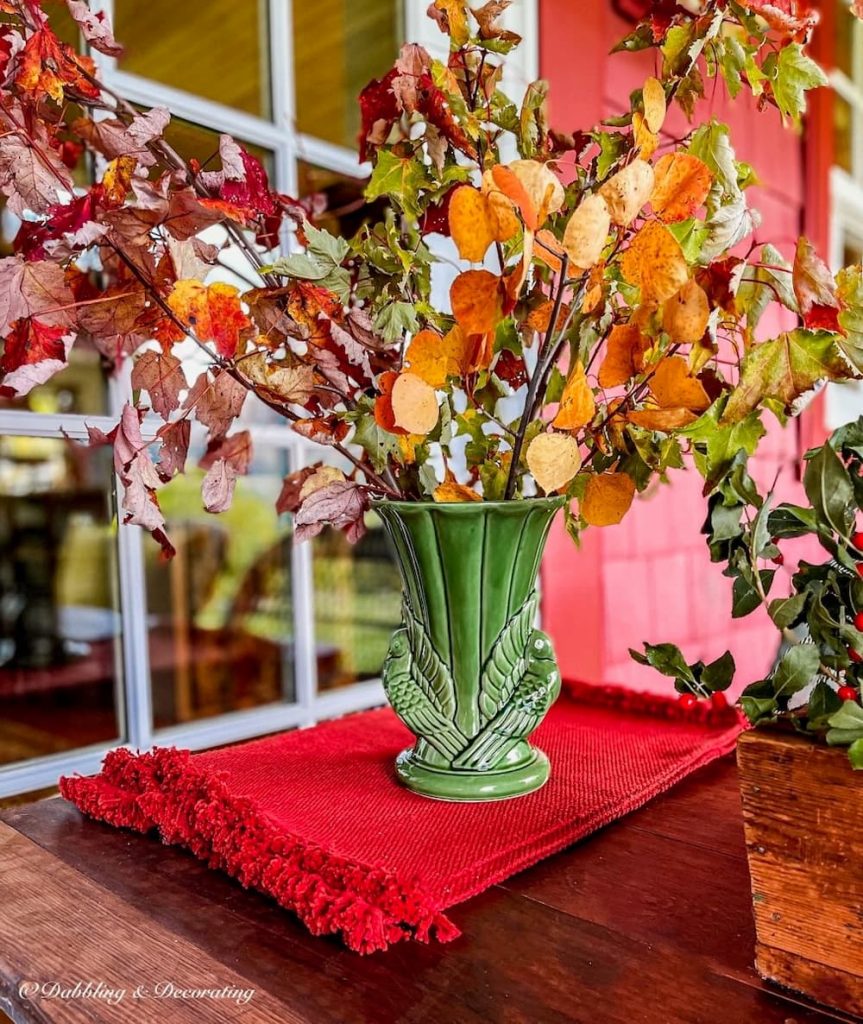 Fall porch table centerpiece with green McCoy vase and colorful foraged branches.