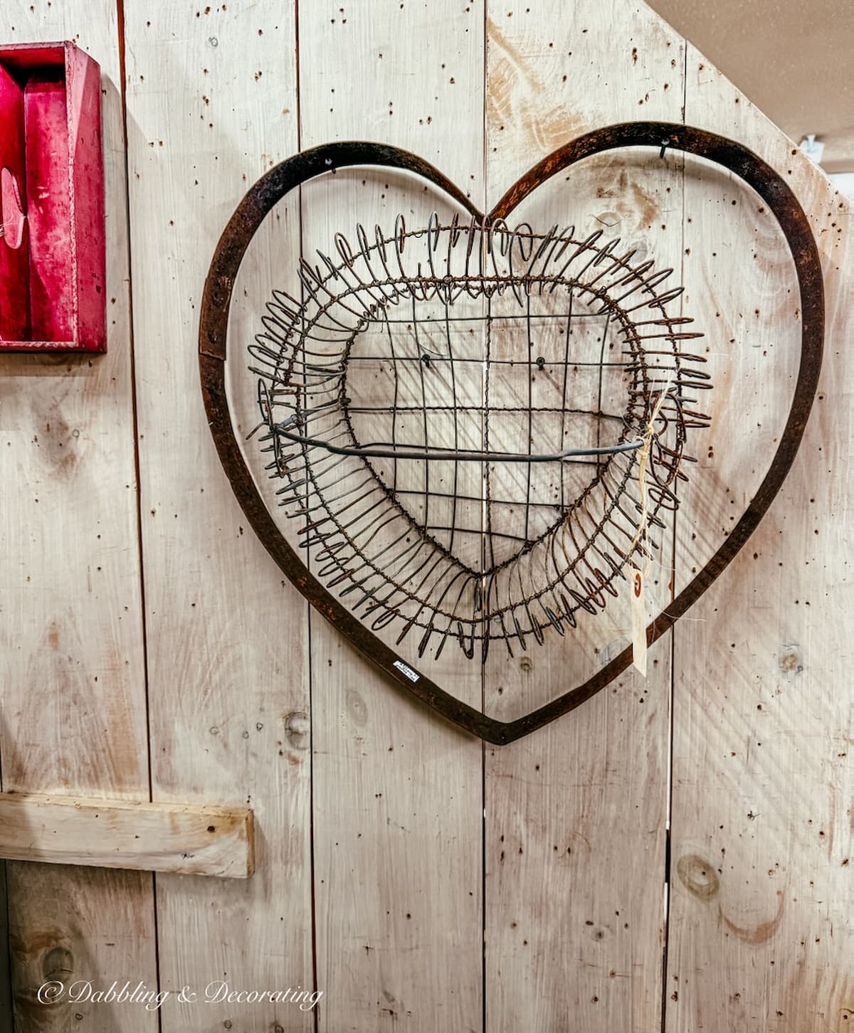 Large metal heart on wall with heart basket hanging inside of it at antqiue store for vintage Valentine' Day decor ideas.
