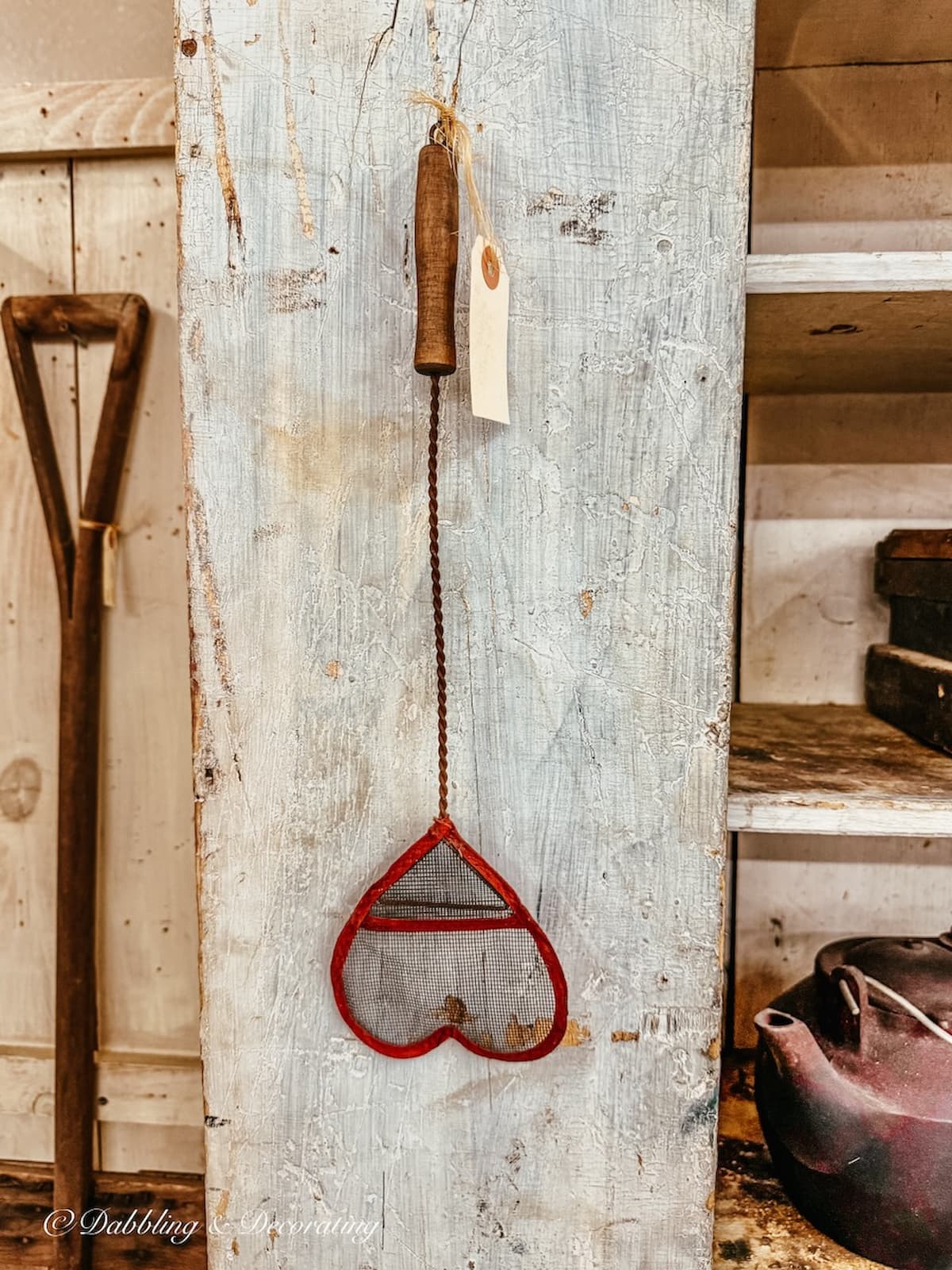 Antique fly swatter in the shape of a red heart hanging on primitive cabinet in antique store for vintage Valentine' Day decor ideas.