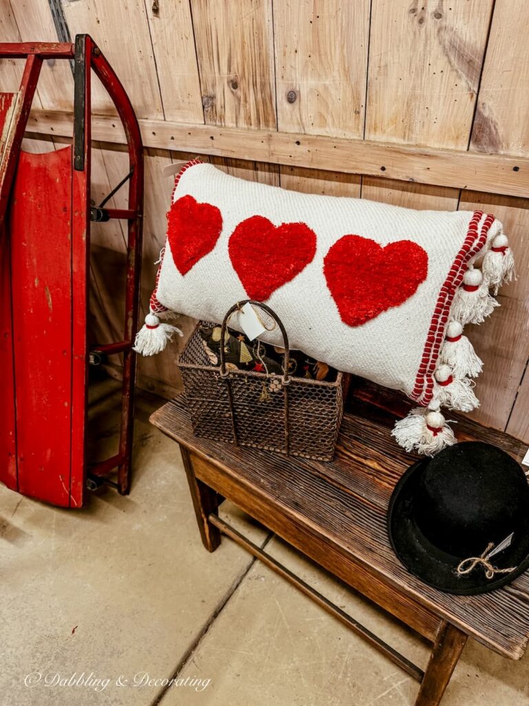 lumbar pillow with three red hearts in antique store next to a red sled on a wooden bench for Vintage Valentine's Day Decor ideas.