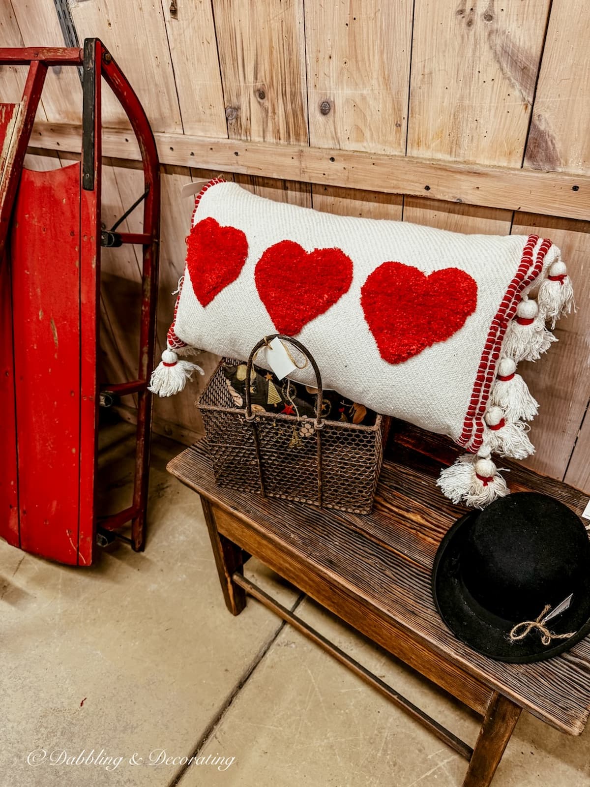 lumbar pillow with three red hearts in antique store next to a red sled on a wooden bench for Vintage Valentine's Day Decor ideas.