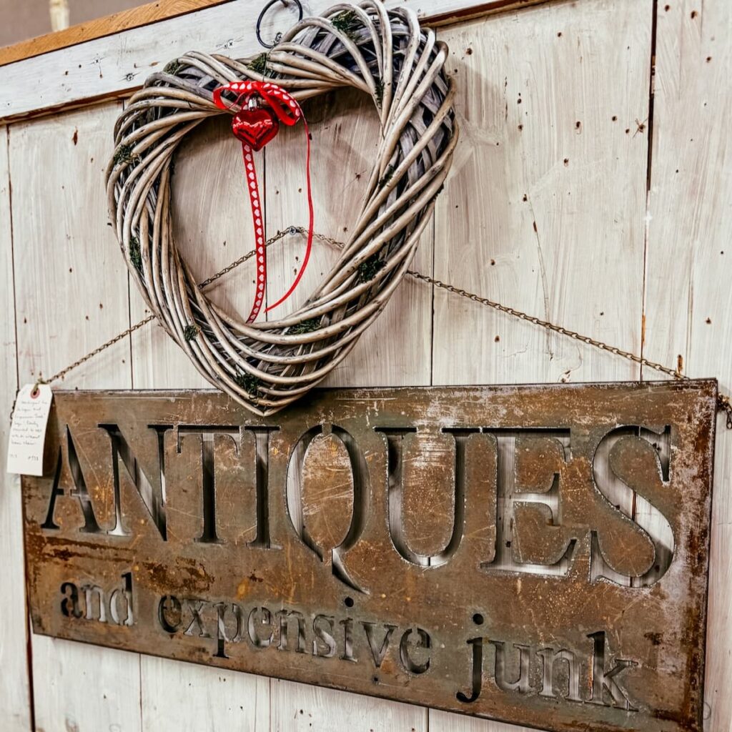 Vintage Valentine's Day decor ideas with a heart grapevine wreath hanging on wall over Antiques rustic sign in antique store.