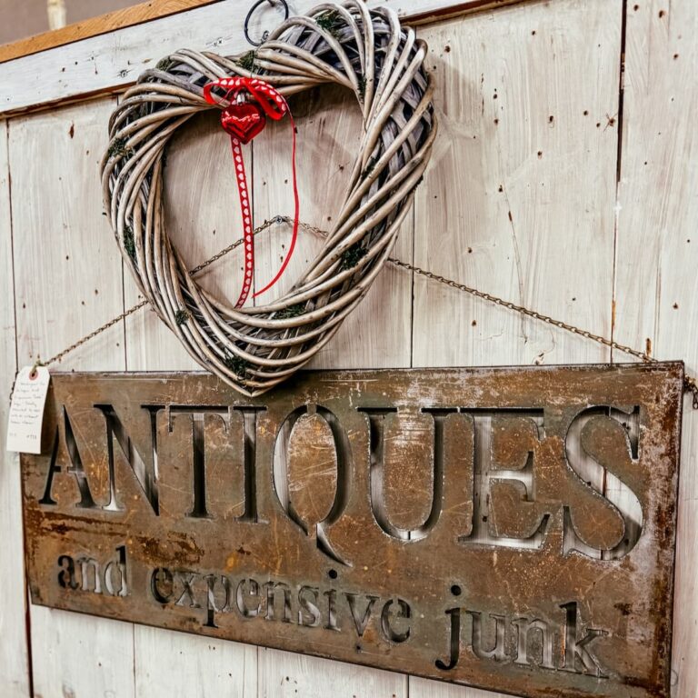 Vintage Valentine's Day decor ideas with a heart grapevine wreath hanging on wall over Antiques rustic sign in antique store.