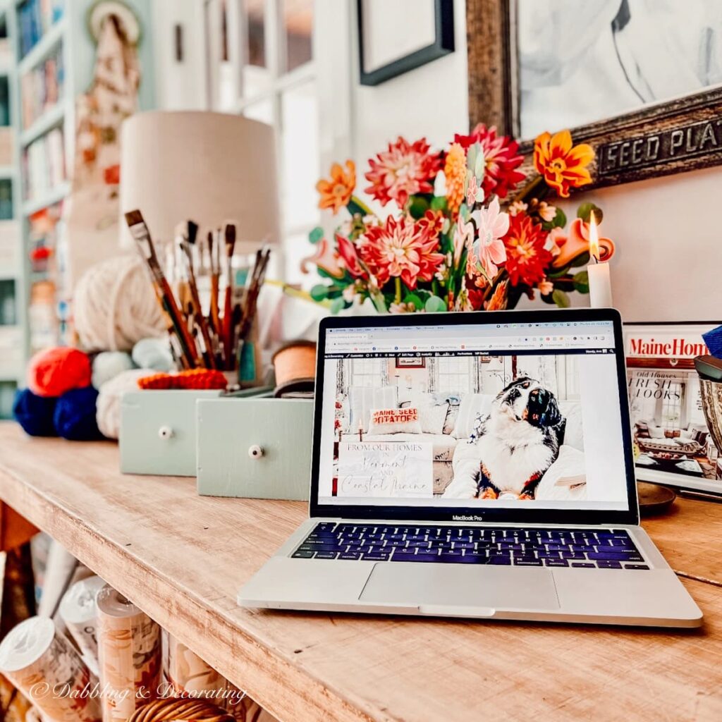 Laptop on vintage eclectic table with craft accessories.