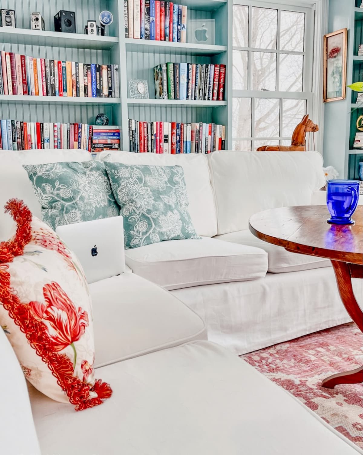 Sunroom craft room ideas with white sectional and bookshelves with eclectic charm along with a pink vintage style rug.
