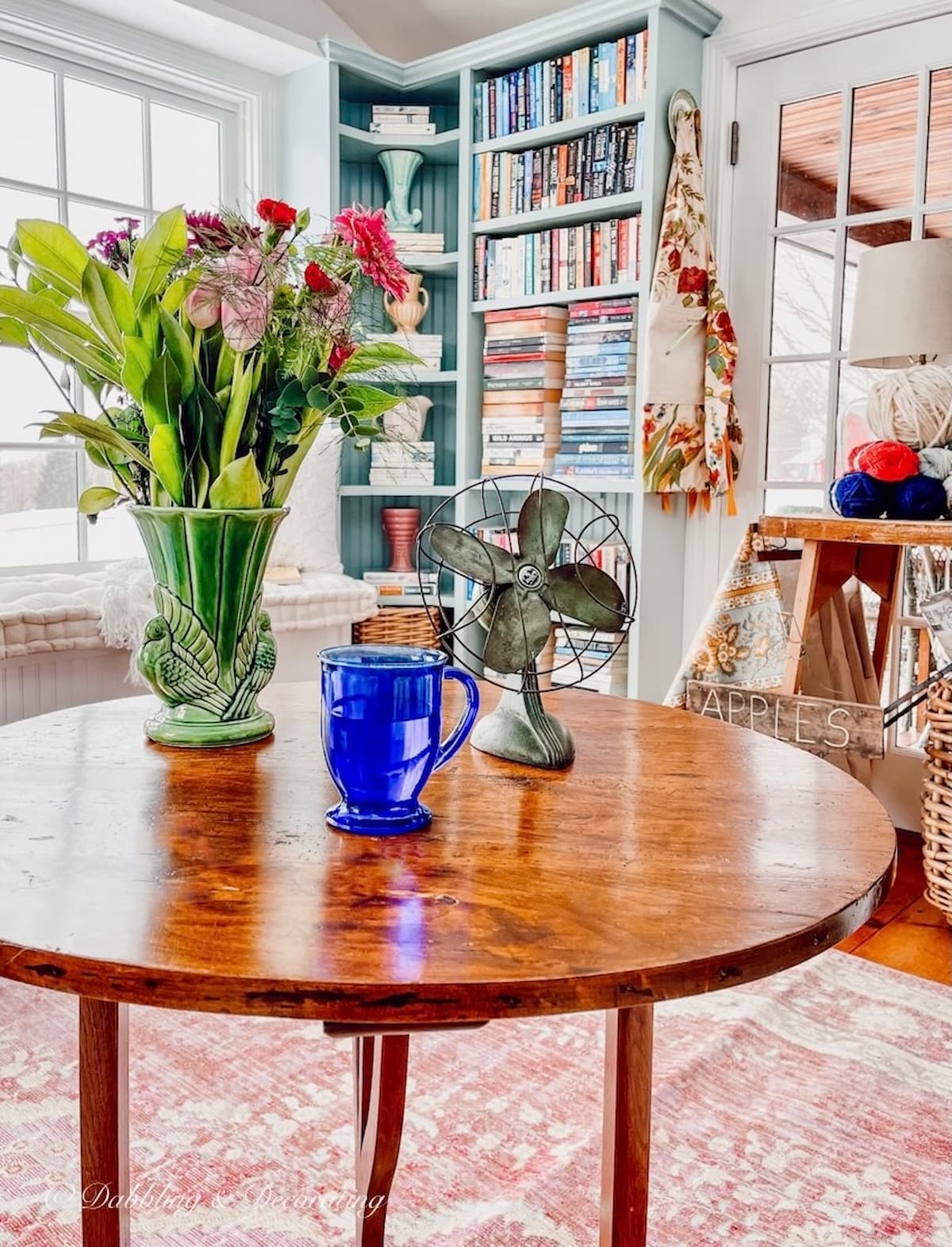 Sunroom craft room ideas with a tall wooden coffee table on a pink rug  with built-in bookshelves.