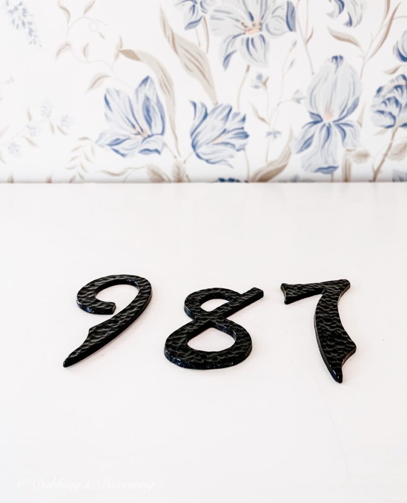 Wrought iron house numbers on white furniture piece.