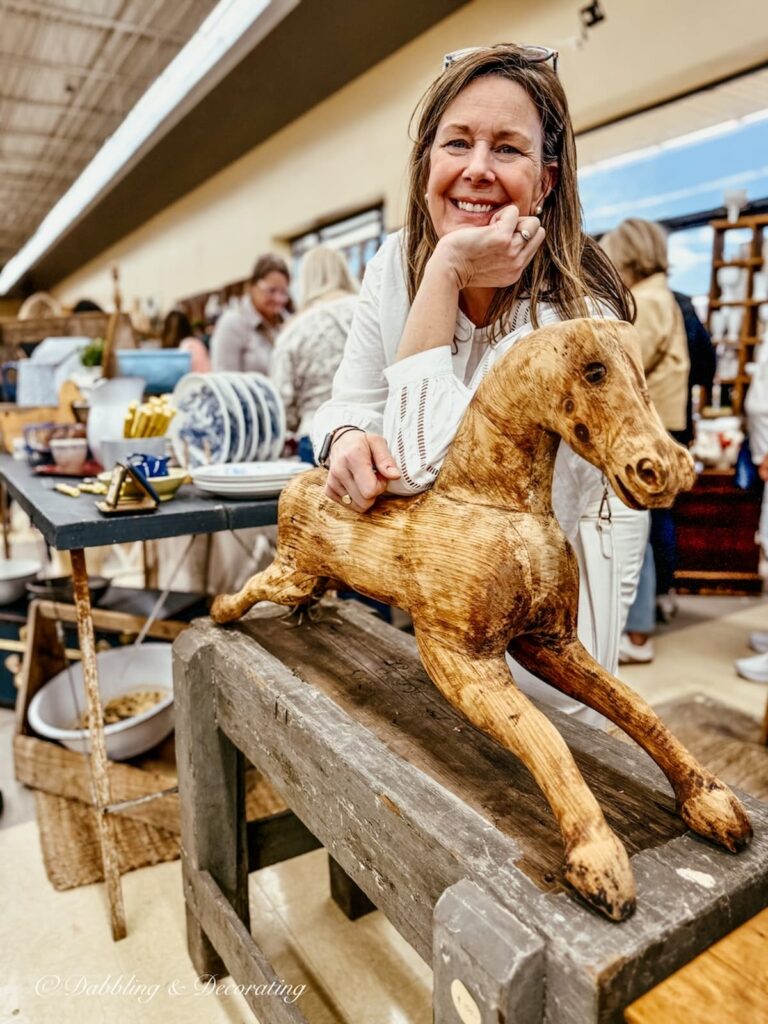 Katherine of Van Claus Designs at Vintage Bazaar New England leaning on a wooden horse in her vintage booth.