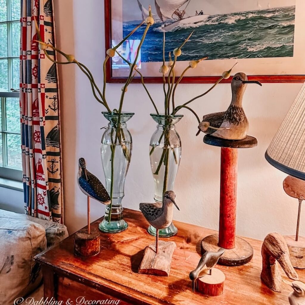 Quaint Nautical Decor Corner with coastal curtains, collection of vintage wooden beach birds on dresser with framed sailboat picture and vases of summer garlic.