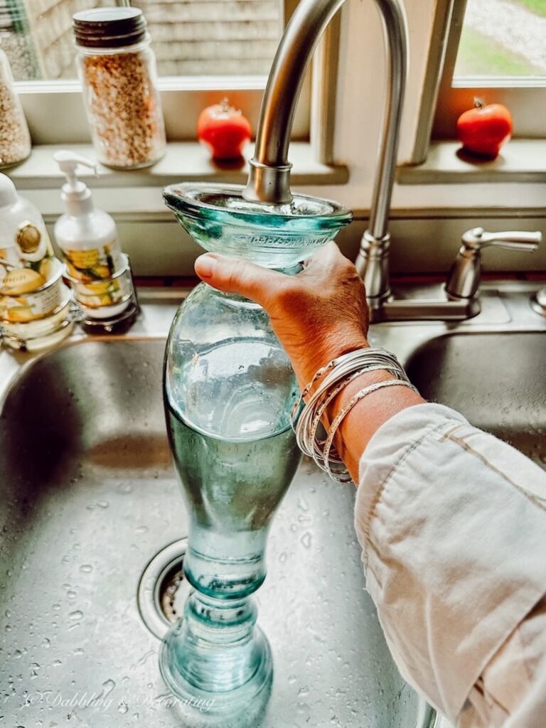 Blue glass vase filling with water in sink.