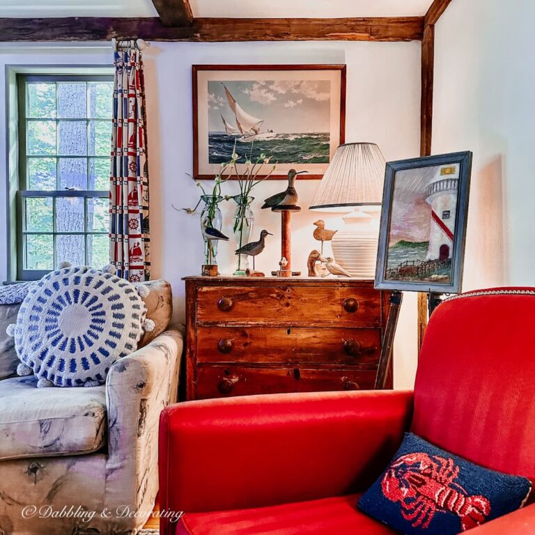Quaint Nautical Decor Corner With primitive antiques including a red chair, wooden dresser and coastal prints.