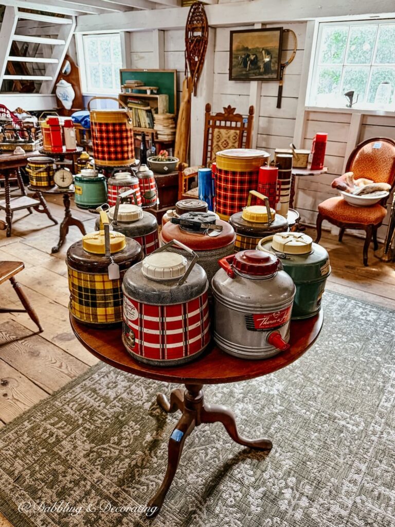 Collection of vintage thermoses inside barn sale with vintage camp collections.