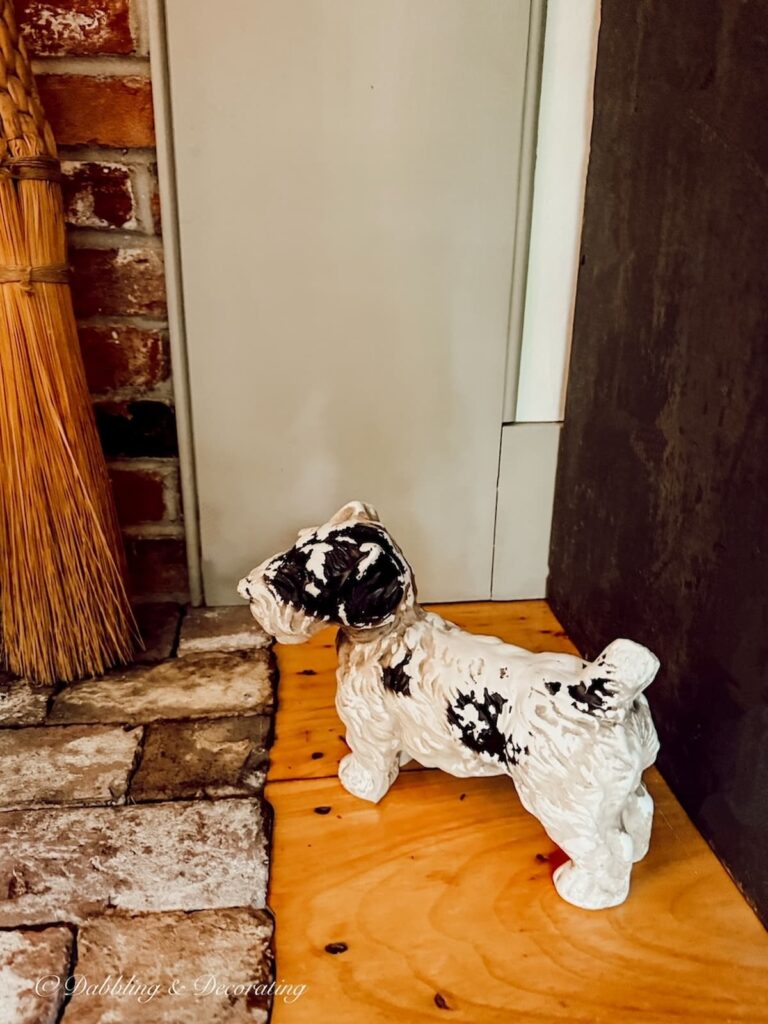 Thrifted chalkware terrier next to brick fireplace hearth.