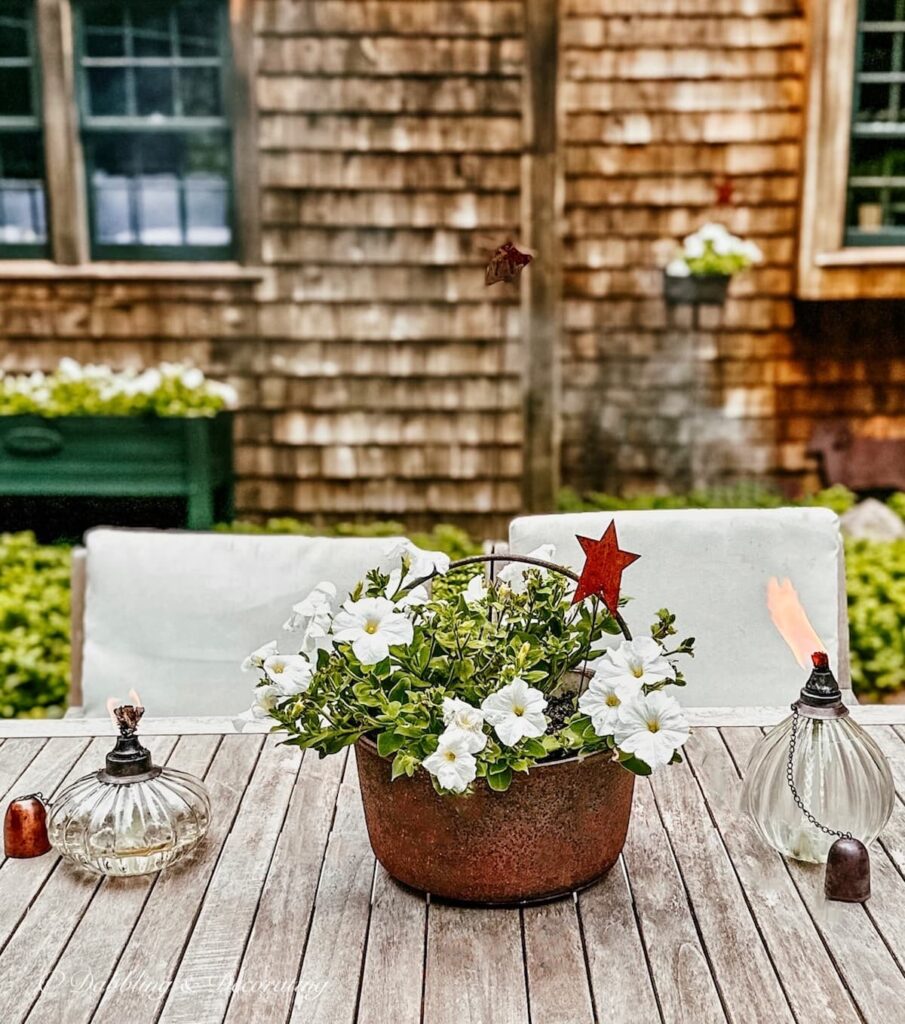 White Petunias Centerpiece in Wrought Iron Planter Pot in front of cedar shake siding home.