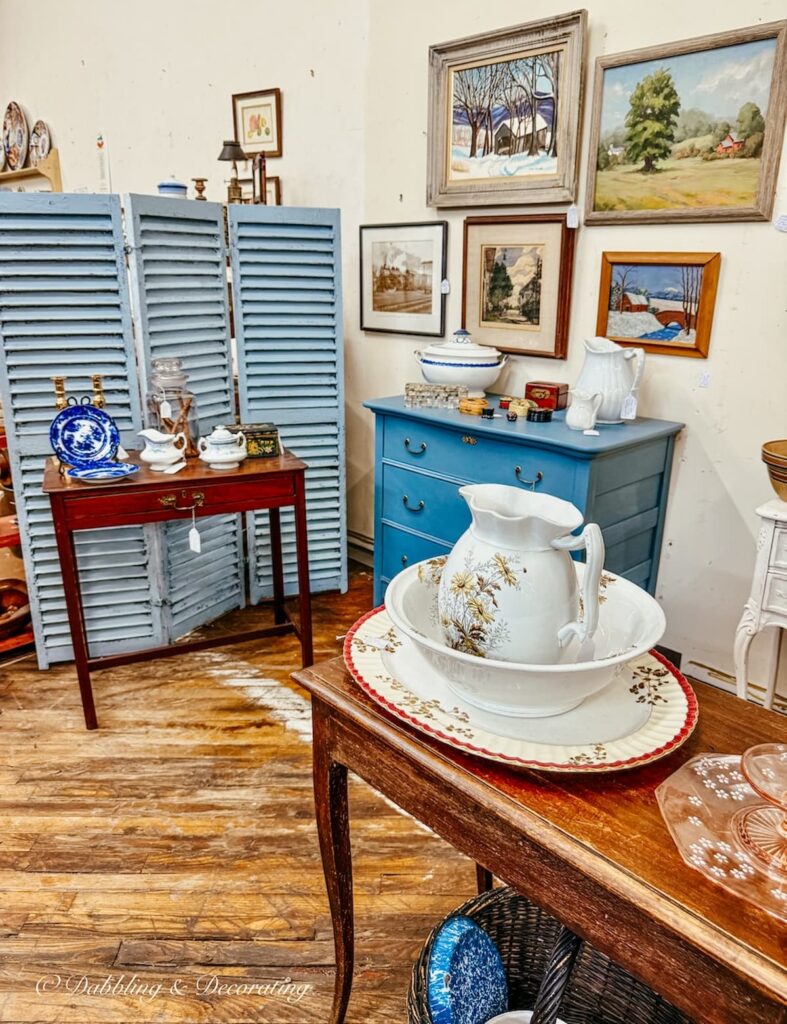 Antique booth inside Cabot Mill Antiques in Brunswick, Maine with blue shutters, dressers, and furnishings.