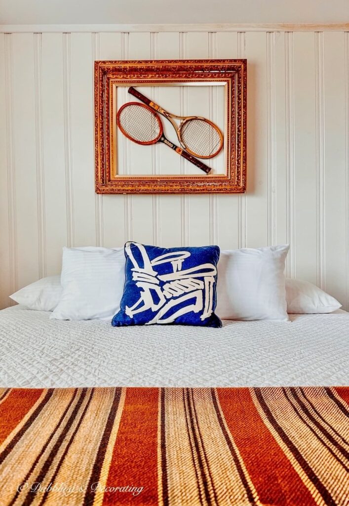 Framed tennis racquets on wall over cottage bed