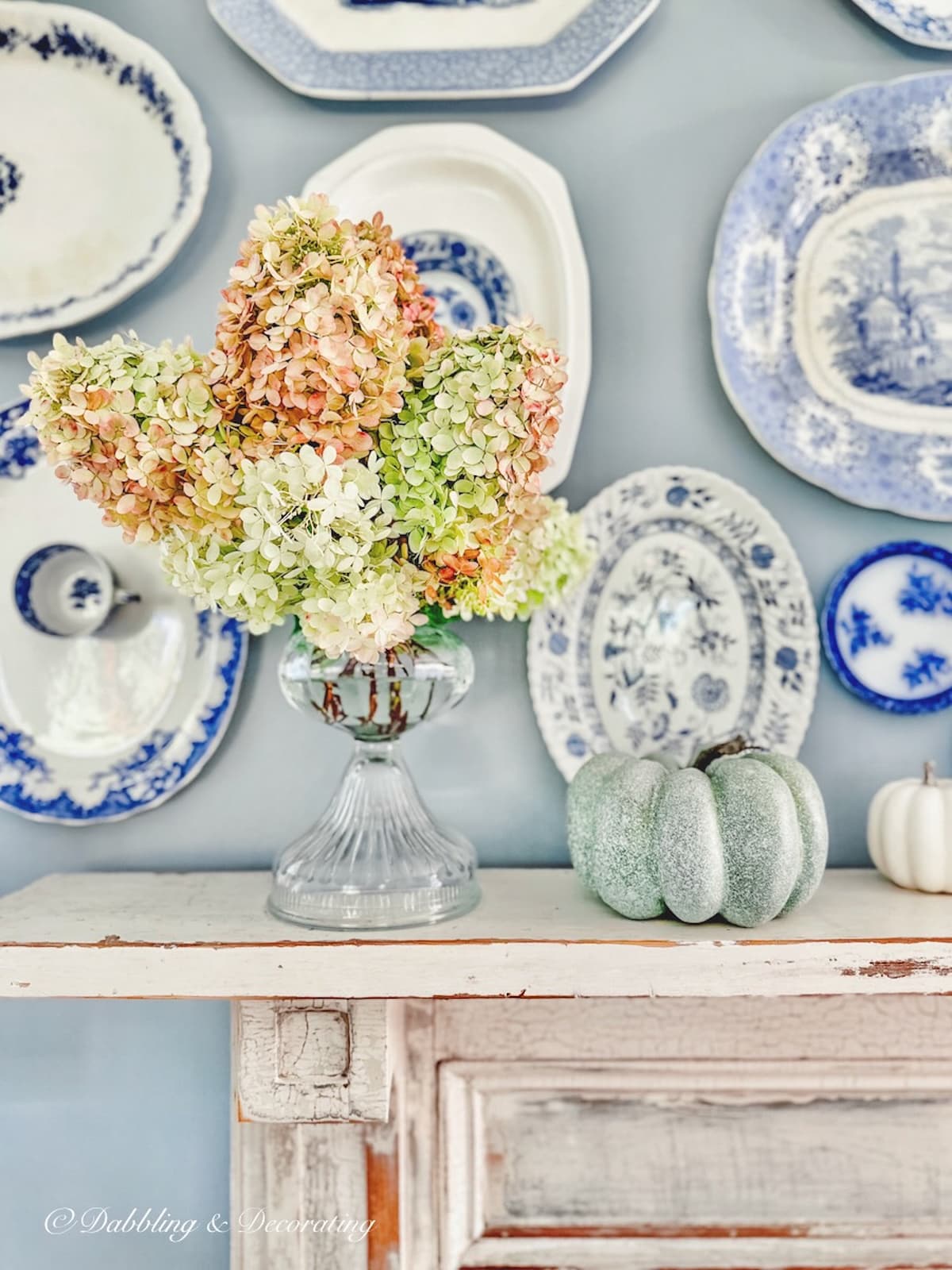 Blue and white fall decor with vintage plate wall over mantel with vintage hydrangeas arrangement and pumpkins.