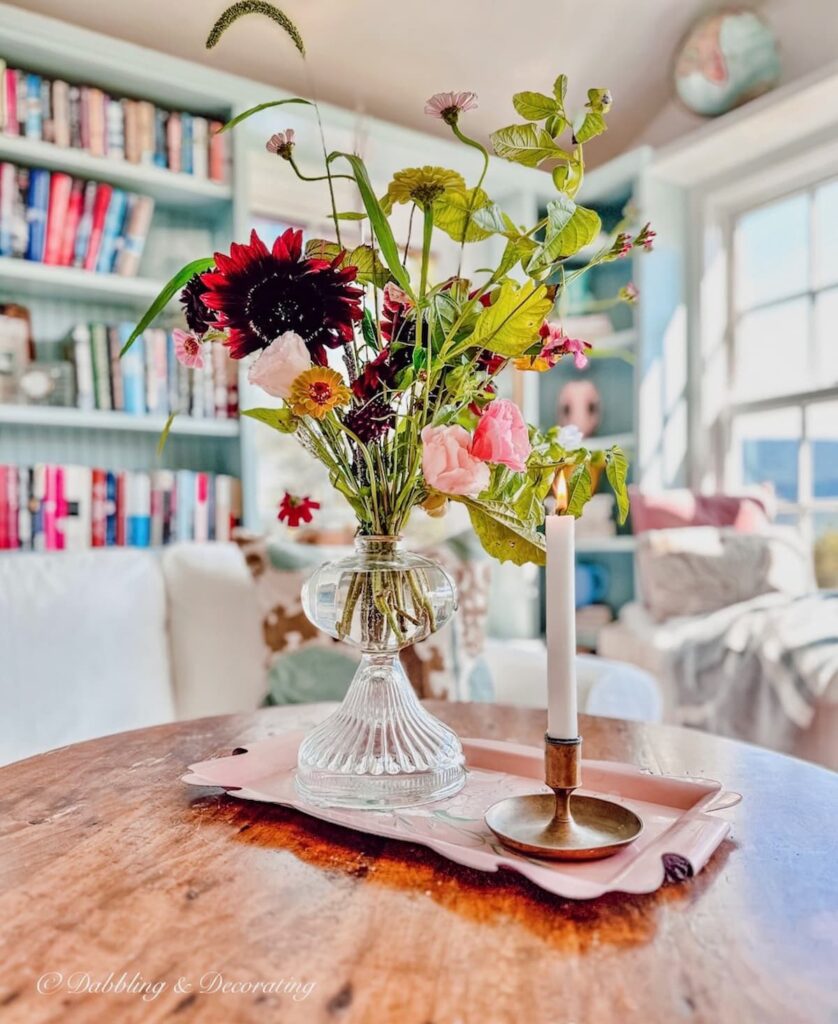 Antique oil lamps with flowers on vintage tray with candle on coffee table in eclectic sunroom.