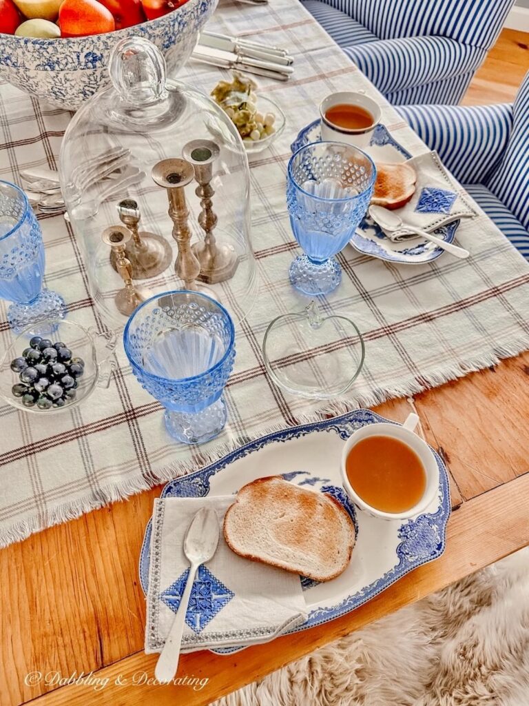 Vintage brass candlesticks under cloche on blue and white table setting with Johnson Brothers Tea and Toast plates.