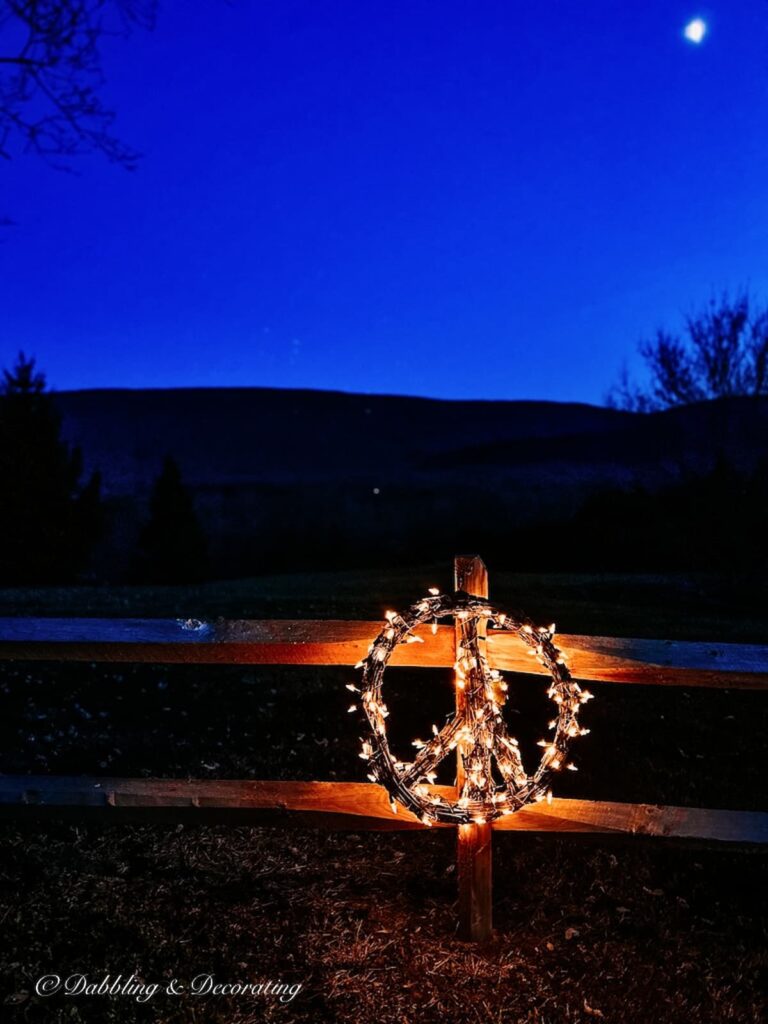 A peace sign is lit up on a fence at night.