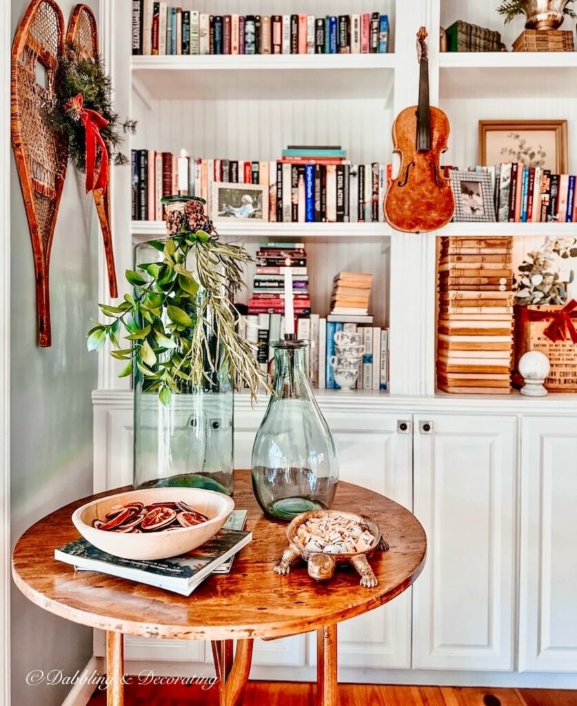 A white kitchen with bookshelves and a table adorned with 12 Days of Christmas Decorations.