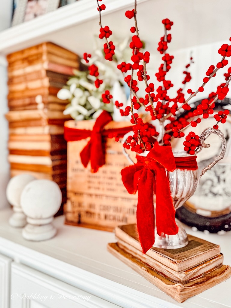 Red berries in a silver vase on a bookshelf adorned with the 12 Days of Christmas Decorations.