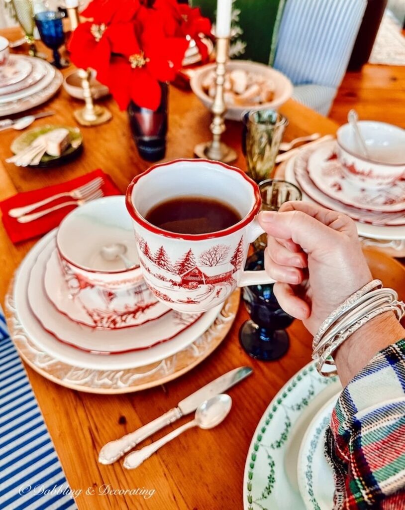 An individual holding a cup of coffee at a table setting adorned with charming cabin decor.