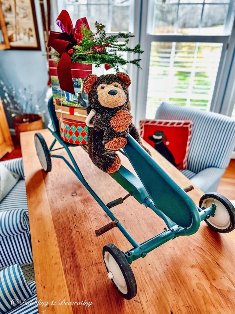 Christmas pedal car with Stuffed Bear and Packages on table.