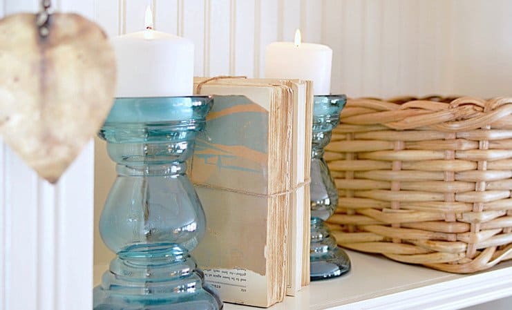 Two blue candlesticks and a basket on bookshelf with vintage old books wrapped in twine between the blue glass candlesticks.