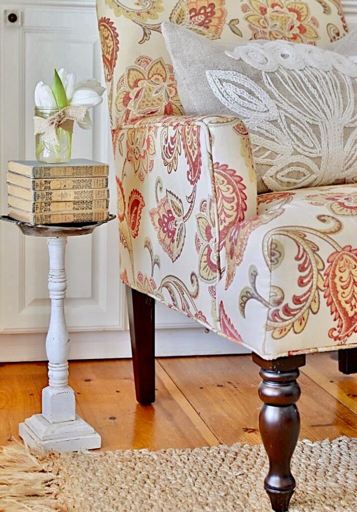 Paisley chair next to a DIY spindle small table with stack of old books and old jar with white tulips.