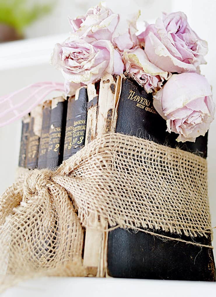 Vintage black books wrapped with burlap bow with dried pink roses wrapped in pink bow in bookshelf styling for Valentine's Day.