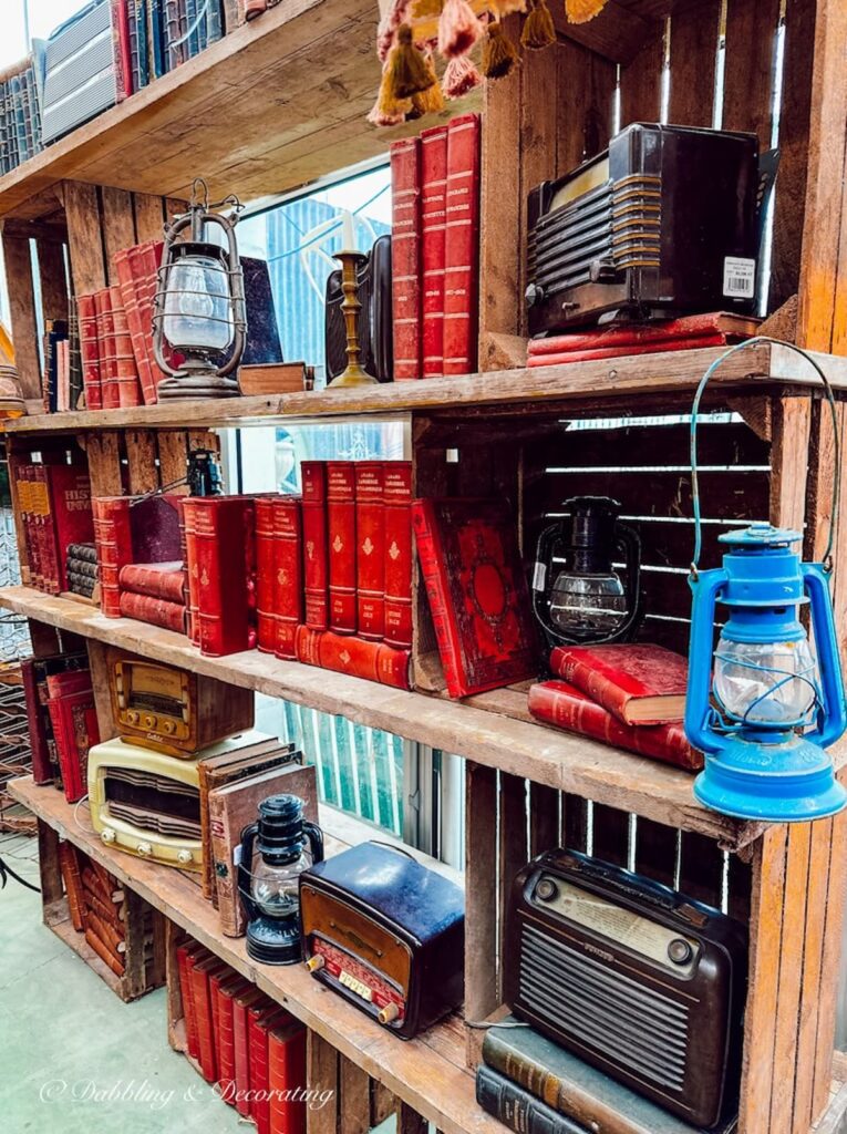 Cabin styled crates and bookshelving at antique store in Paris with old radios and lanterns and old red books decorating ideas.