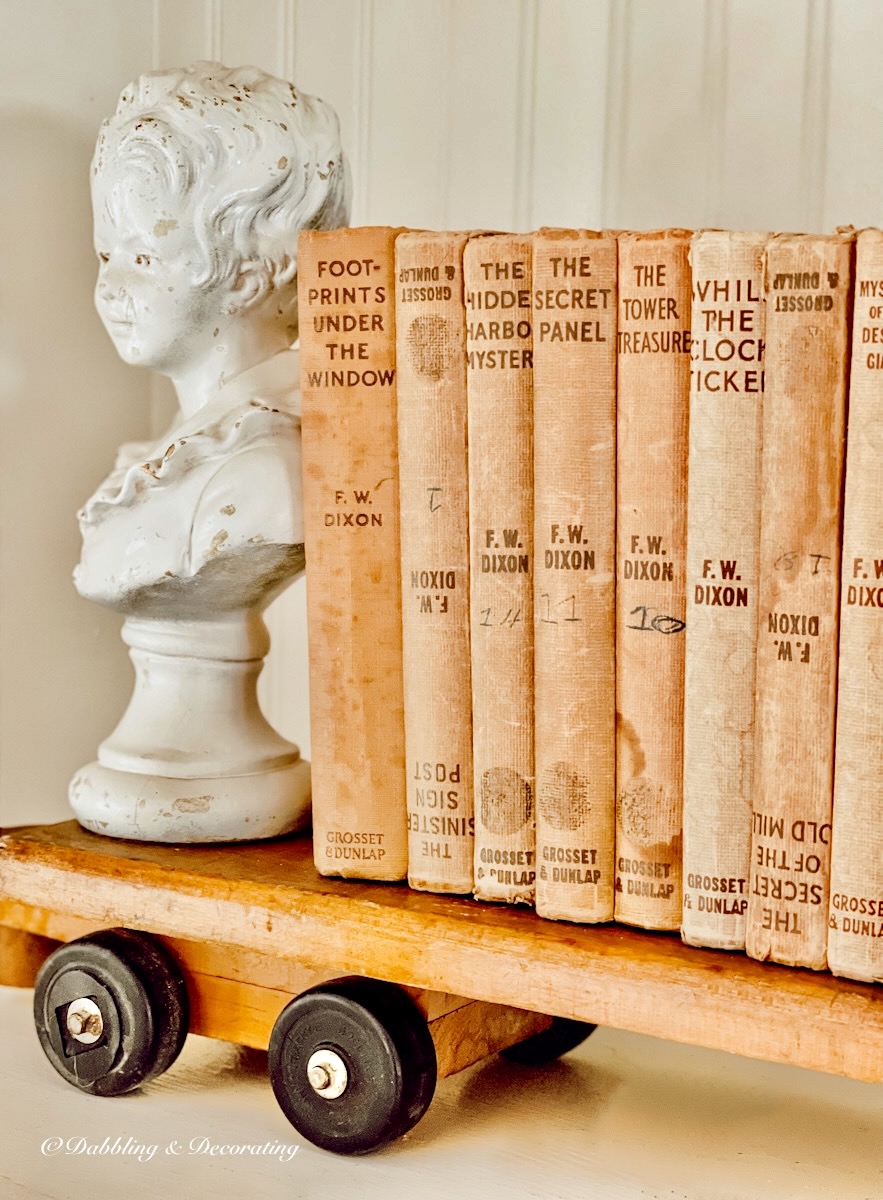 Vintage neutral books on old wooden train with white antique busts as bookend on bookshelf.