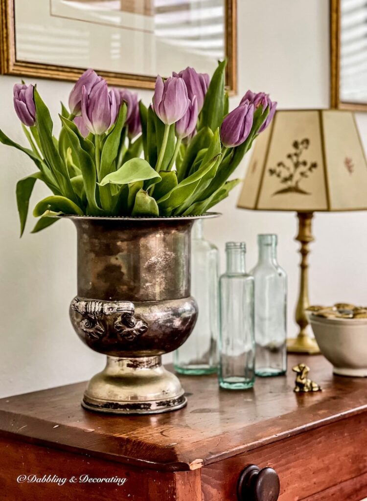Purple tulip arrangements in a vintage silver champagne bucket on antique wooden table.