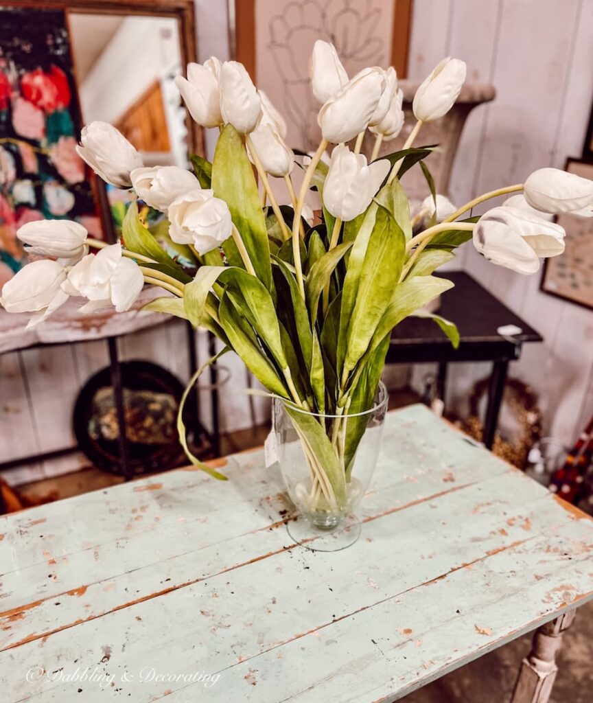 Glass vase with bouquet of white tulips on antique table.