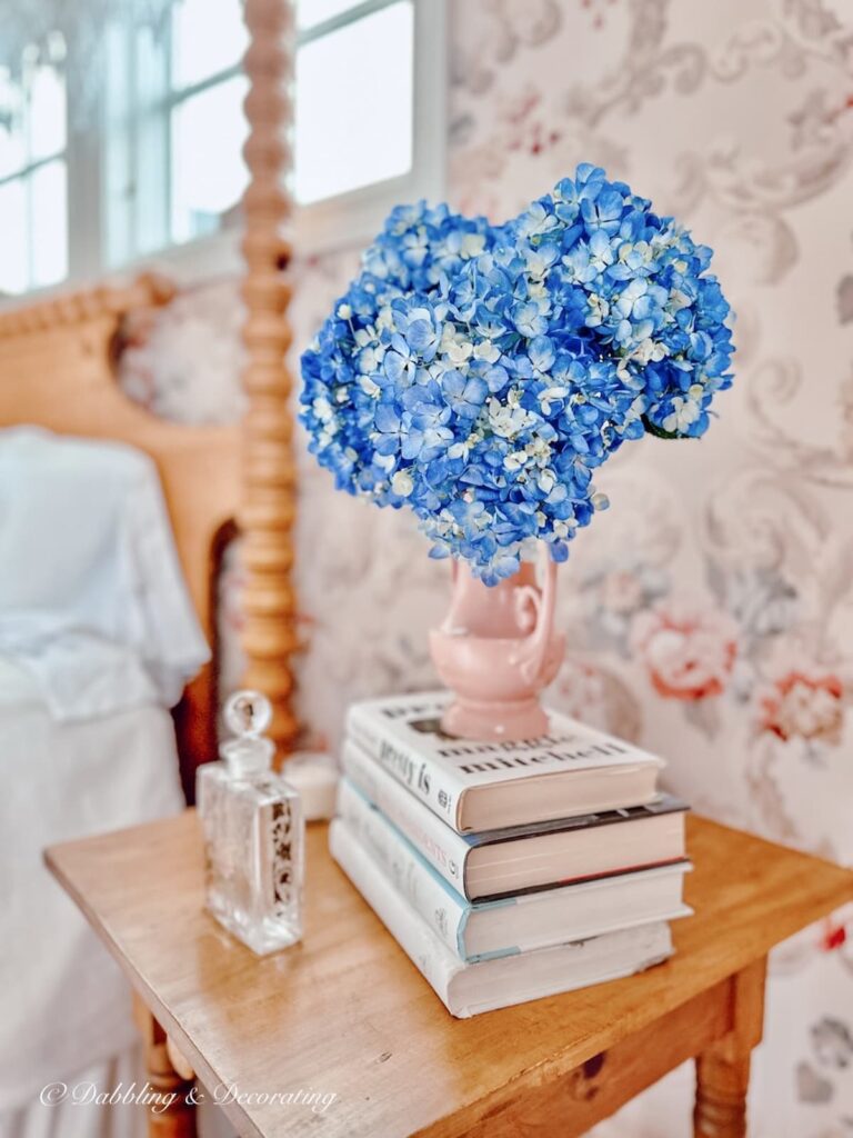 Bedroom side table with old books stacked with floral bouquet.