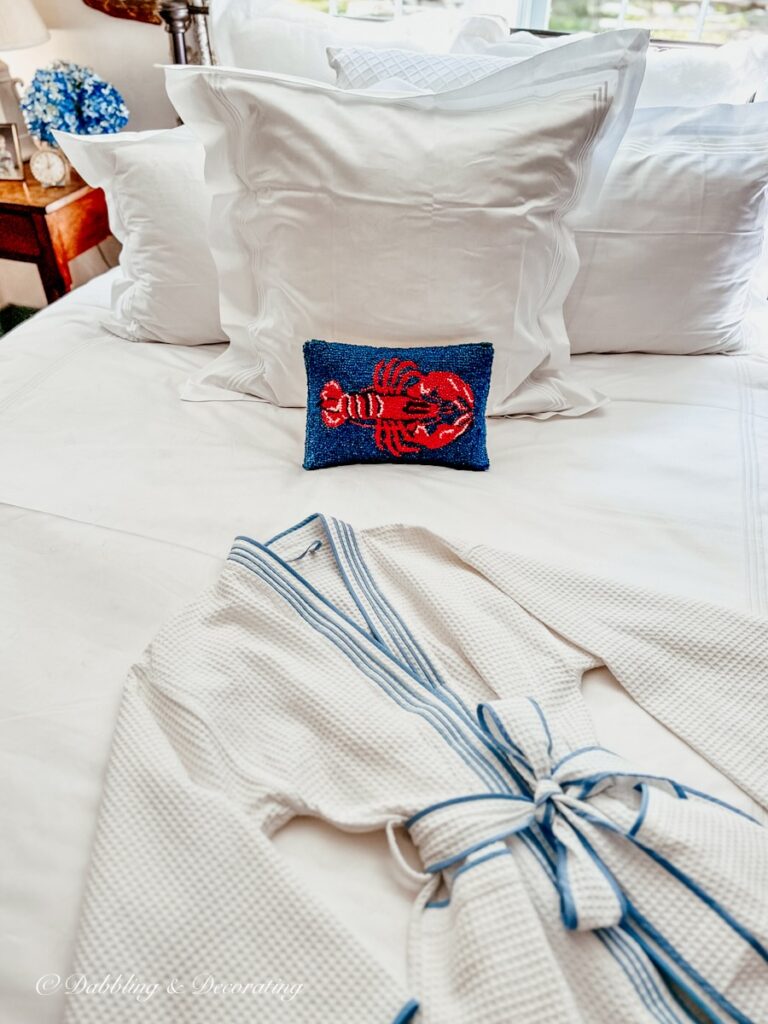 Schweitzer Linen's Hampton Court Bedding in all white with light blue trim and matching bathrobe with one lobster pillow in coastal bedding ideas for beach houses.