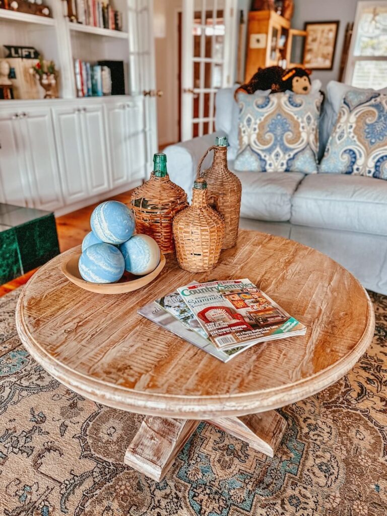 Demijohns on coffee table with magazines and wooden bowl of blue bowling balls.