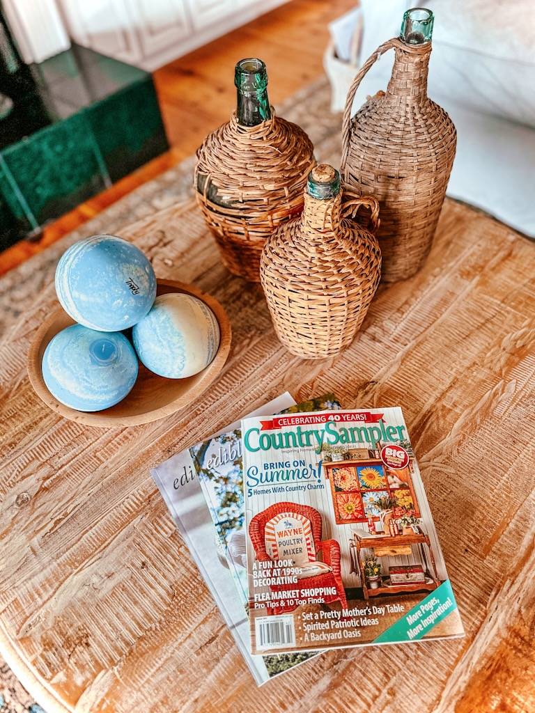 Demijohns on coffee table with magazines and wooden bowl of blue bowling balls.