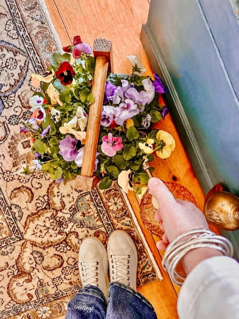 Box of pansies on floor getting watered in a strawberry container in cottage farmhouse decor ideas.