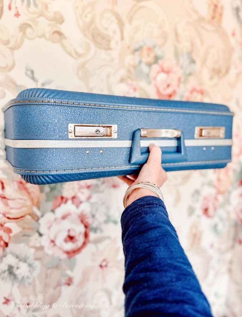 Vintage blue suitcase shelf on wallpapered wall.