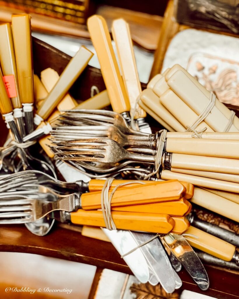 Sets of Bakelite flatware at flea market with orange and white handles.