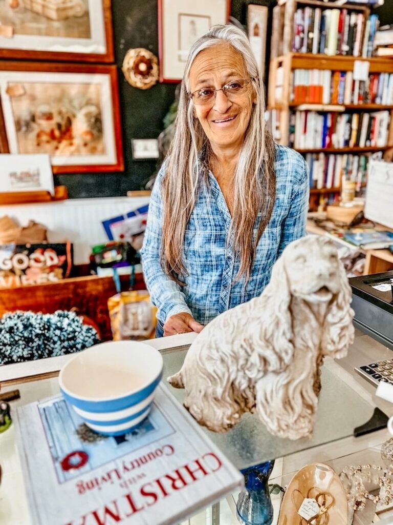 Woman at check out counter at Second Chance thrift Shoppe with Dog garden statue and cornishware, Vintage Home Decor Finds.