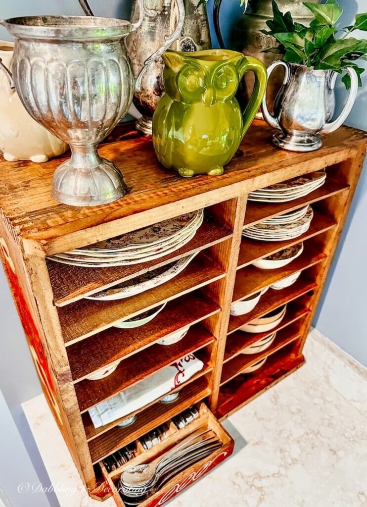 Vintage pie safe cabinet on kitchen counter with vintage dishes and pitchers displayed throughout.