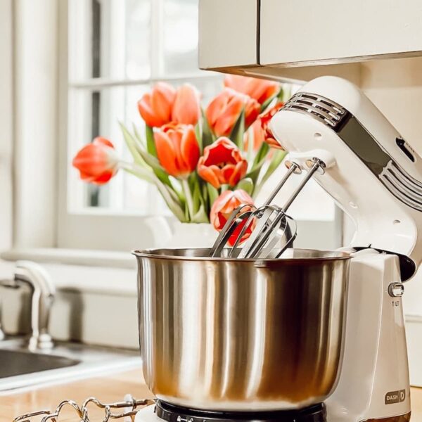 White baking mixer on wooden kitchen counter with pink tulips.