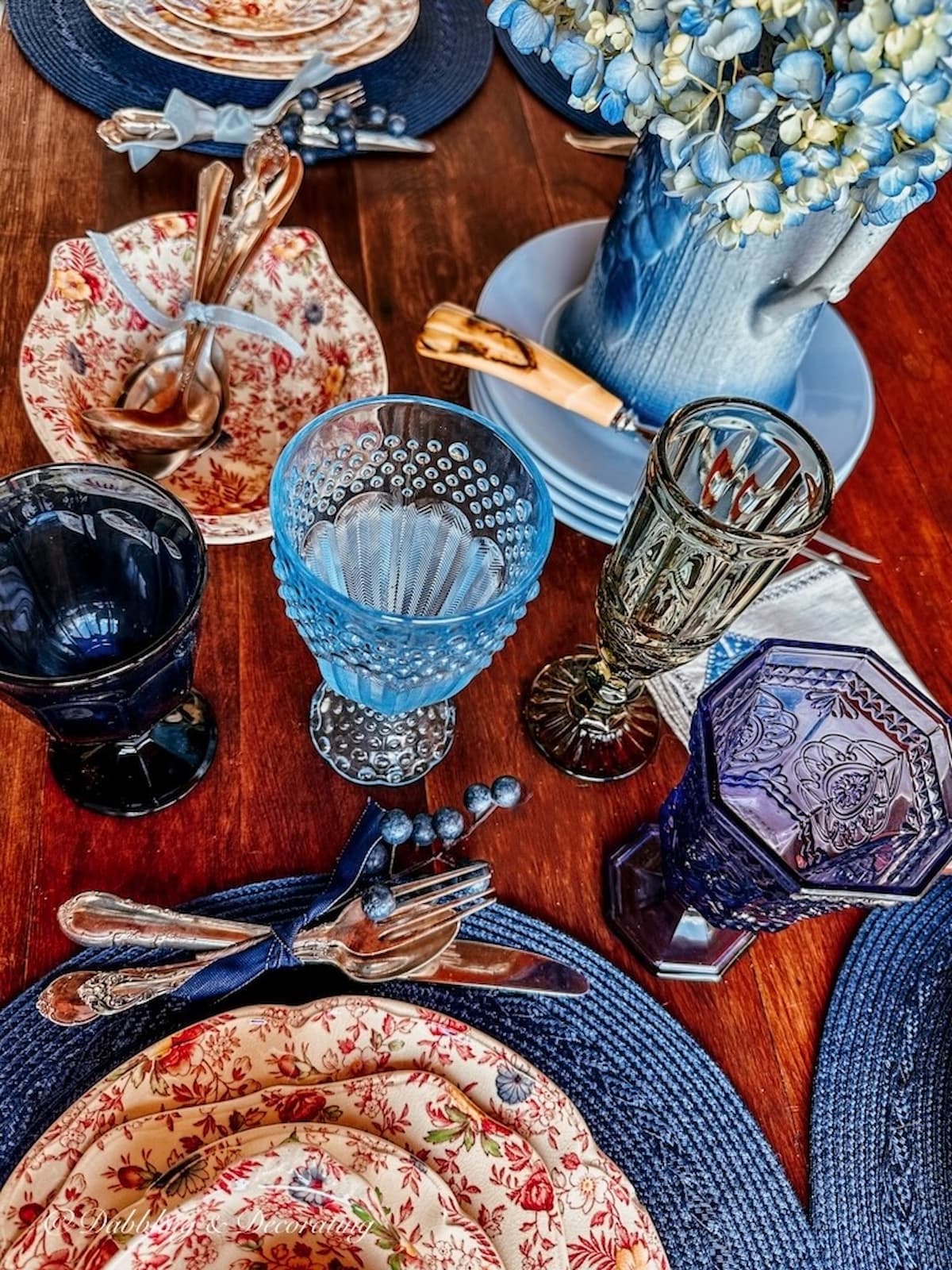 Fall tablescape with Johnson brother's Chintz dishes, colored glassware and vintage silverware on blue placemats.