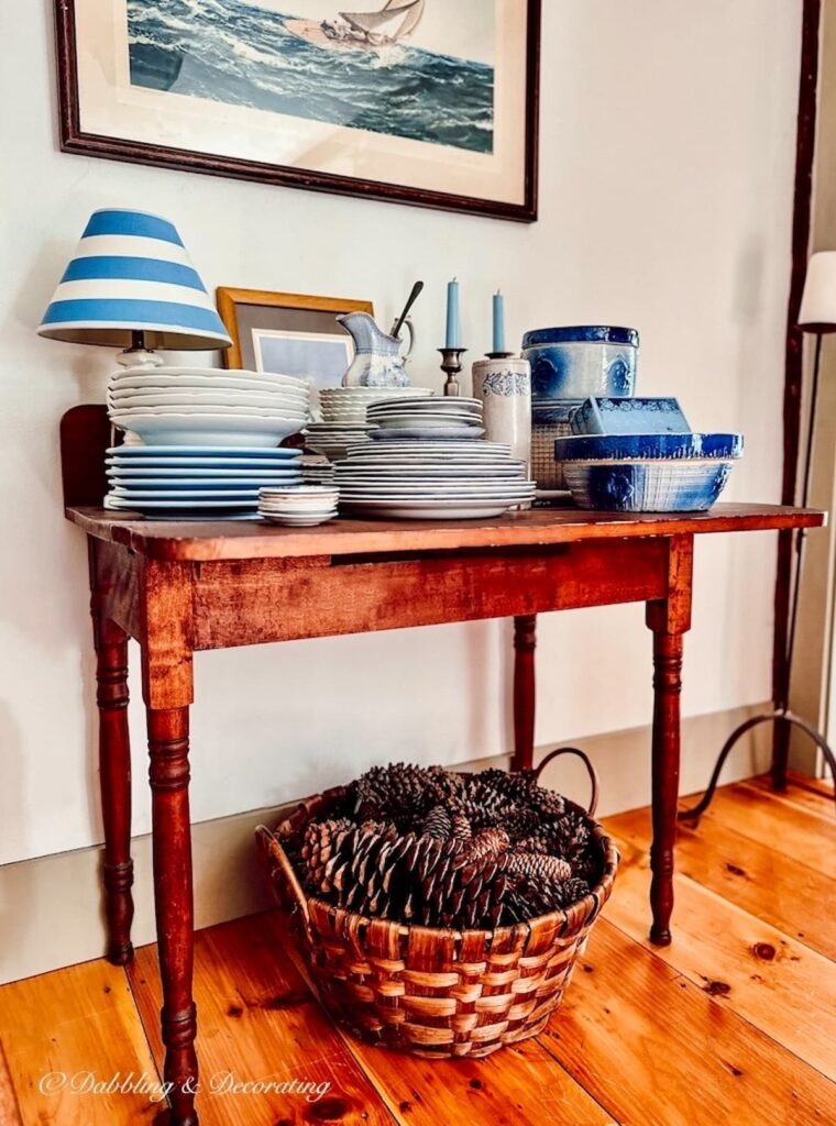 Basket of pinecones under antique table filled with blue and white vintage dishwares.