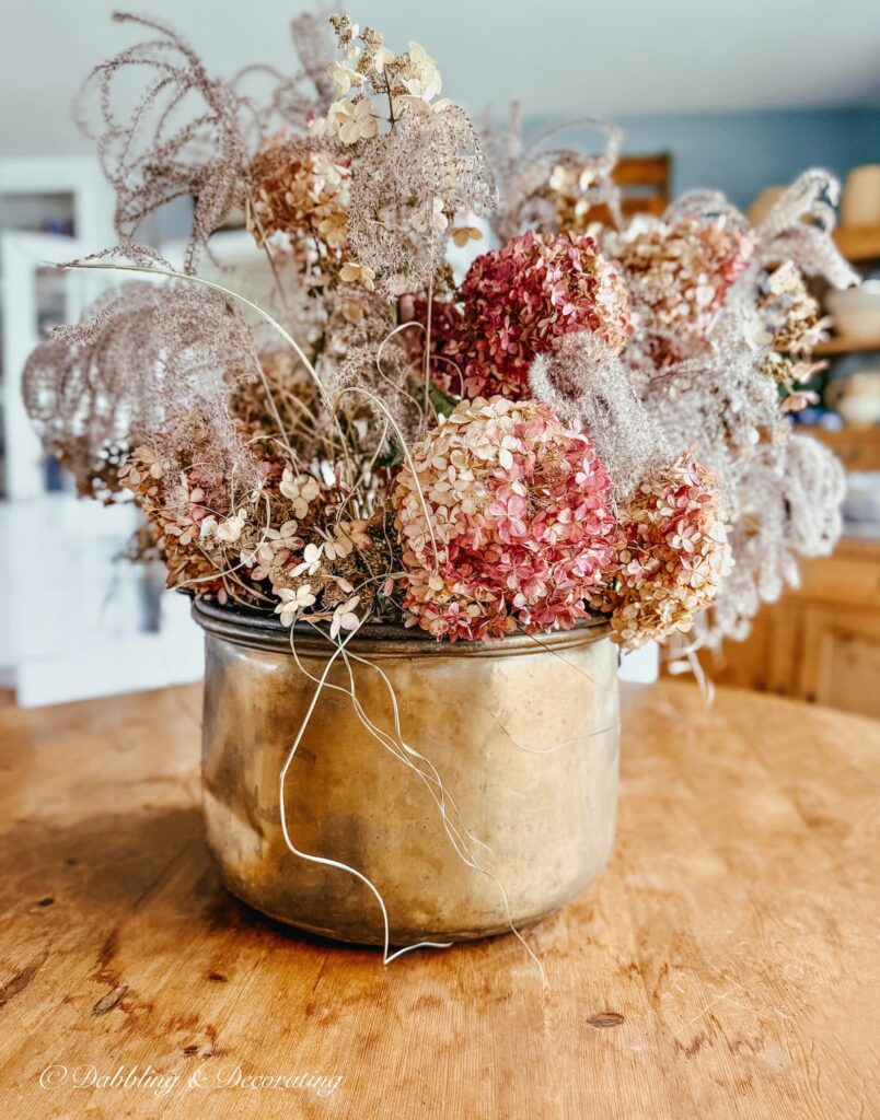 Beautiful fall pink fall hydrangea arrangement in large copper pot on vintage dining room wooden table.