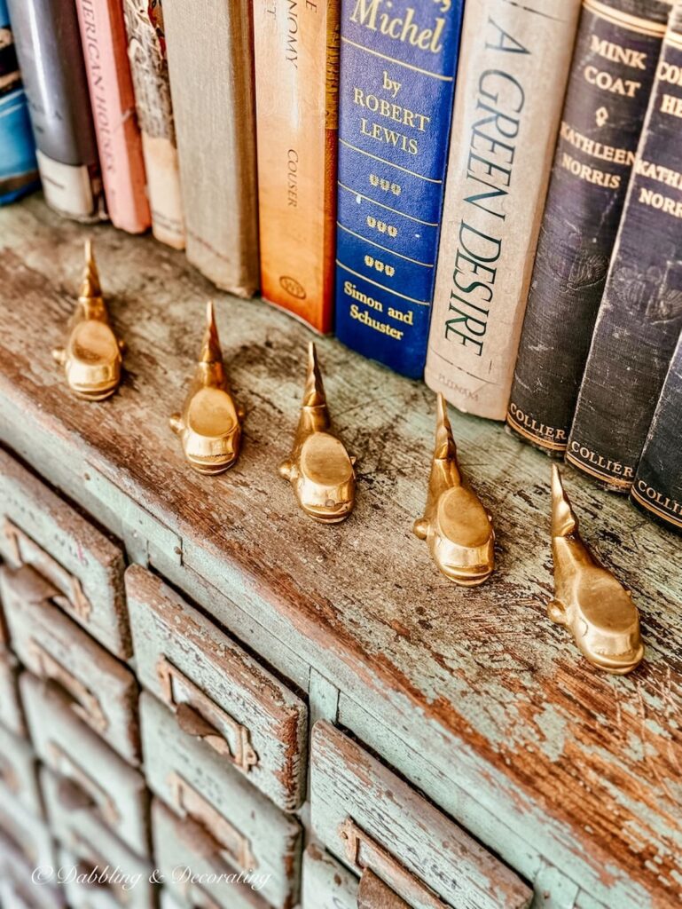 5 brass whale knife rests on apothecary cabinet.